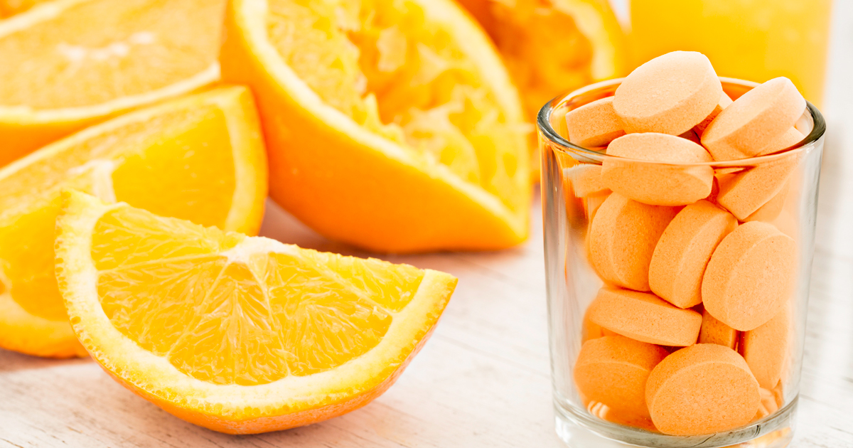 Quartered orange slices next to a cup full of vitamin C tablets
