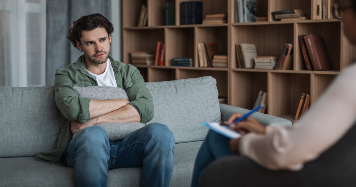 Man holding a pillow, sitting on couch in counselor's office