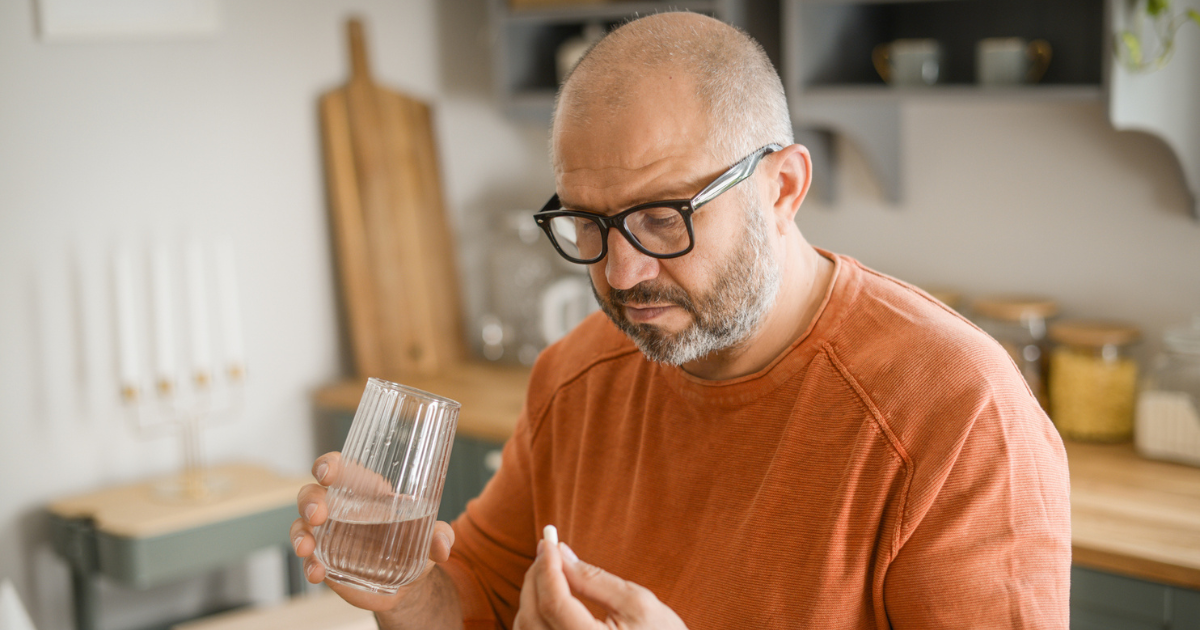 Man holding a pill and a glass of water