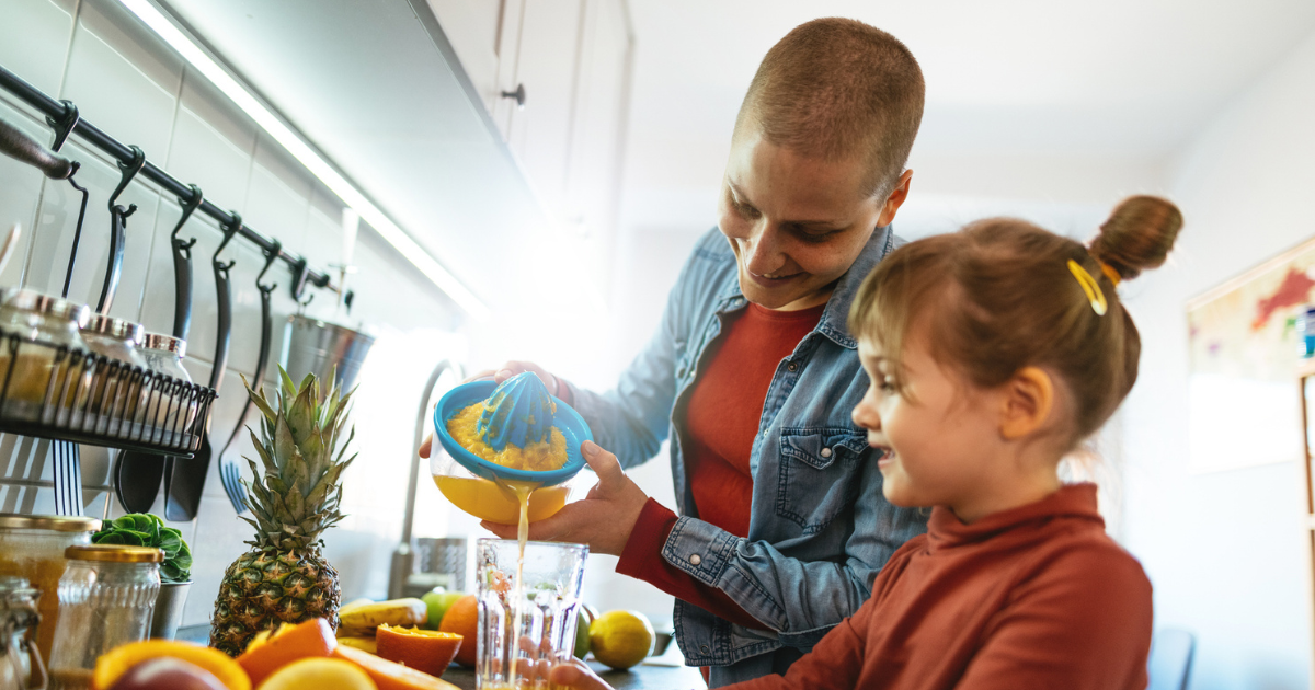 Woman with cancer juicing fruit with young daughter