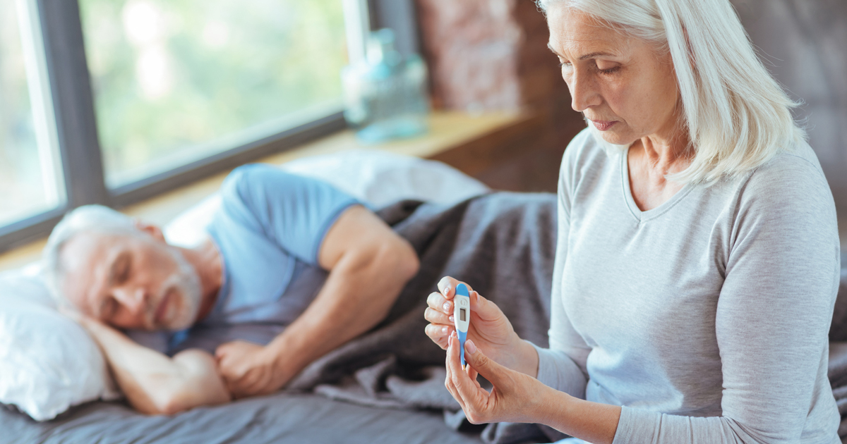 Sick man lying down and woman holding thermometer