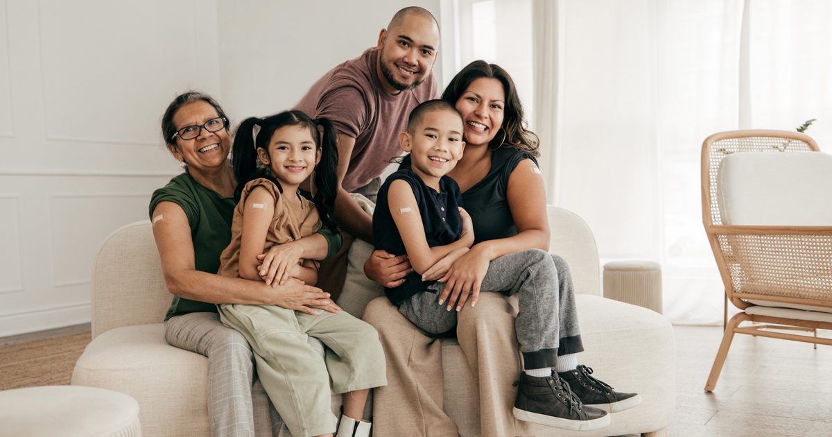 Family with a grandmother, mother, father, daughter, and son sitting together on a couch with bandaids on their arms