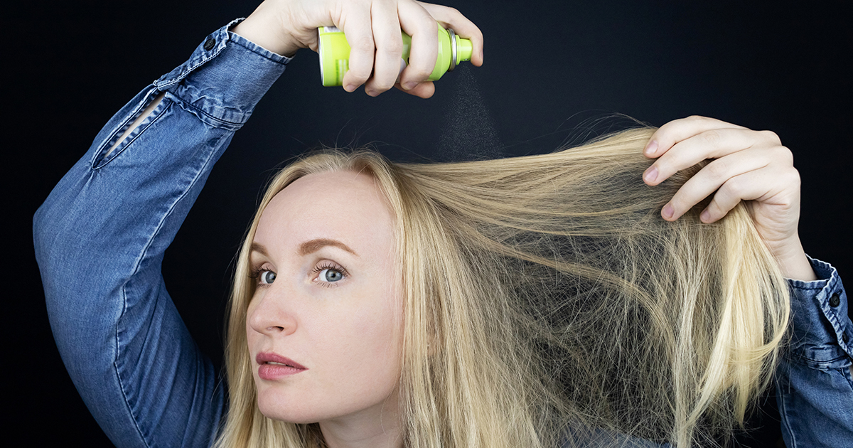 woman spraying her hair with dry shampoo