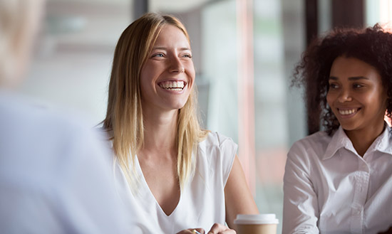 Two women smiling and talking over coffee. 