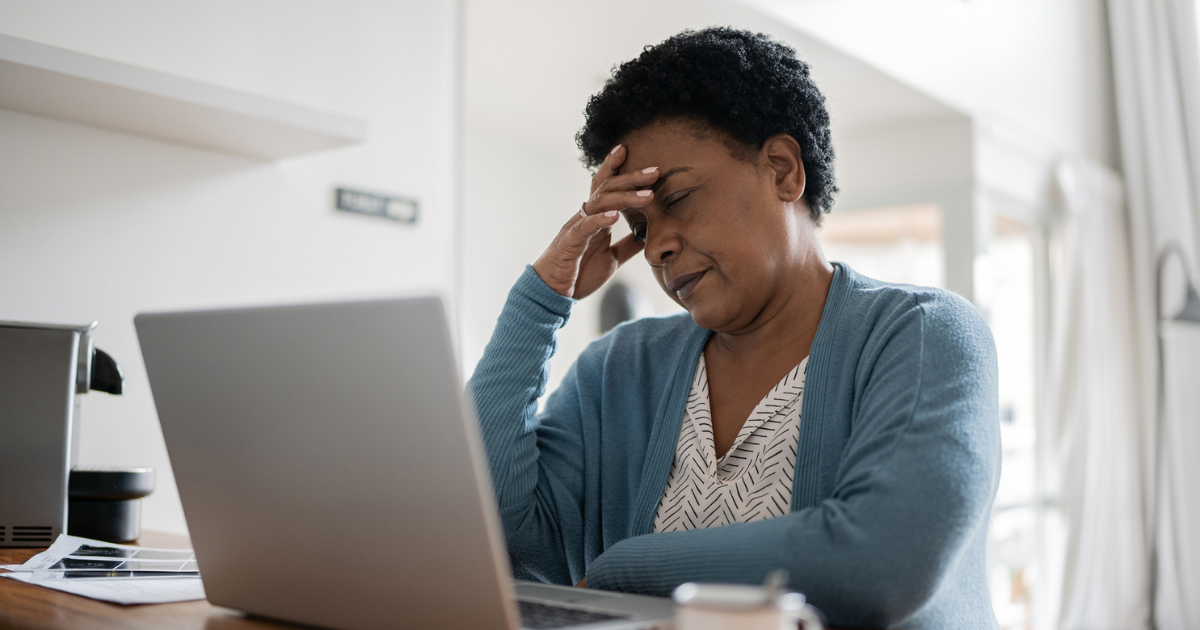 Woman sitting in front of her laptop and holding her head in pain