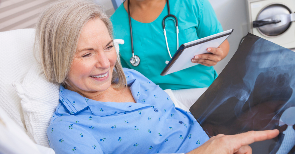 Woman in hospital bed looking at x-ray of hip replacement