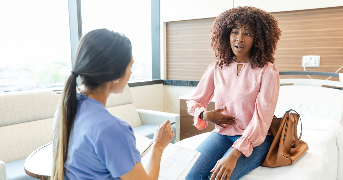 Woman holding her stomach in pain, talking to nurse