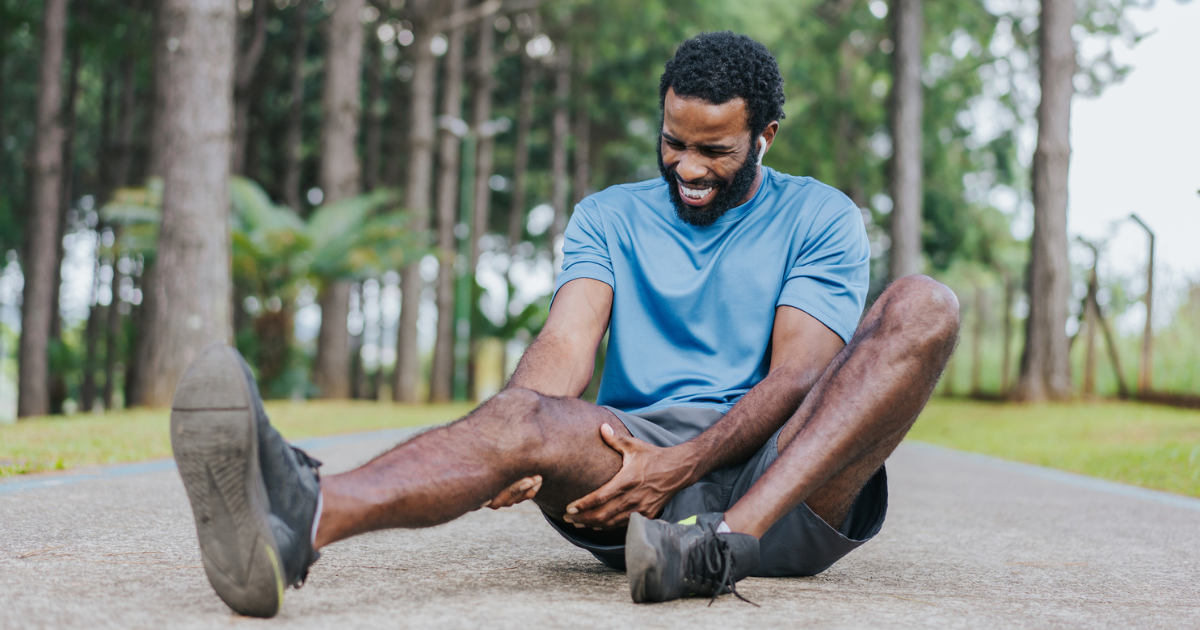 Man sitting on the ground holding his thigh in pain