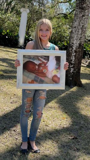 Braylynn, age 9, holding a photo of when she was a baby