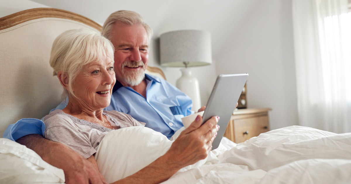Older couple sitting in bed, looking at a tablet