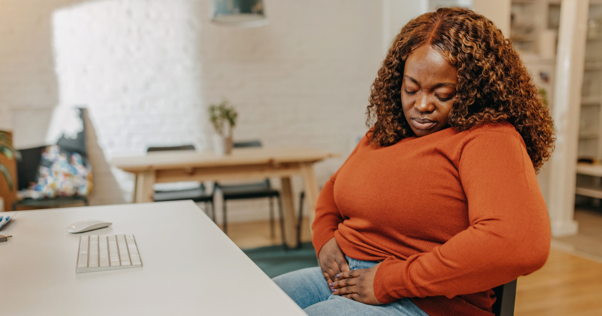 Woman sitting at desk holding abdomen in pain