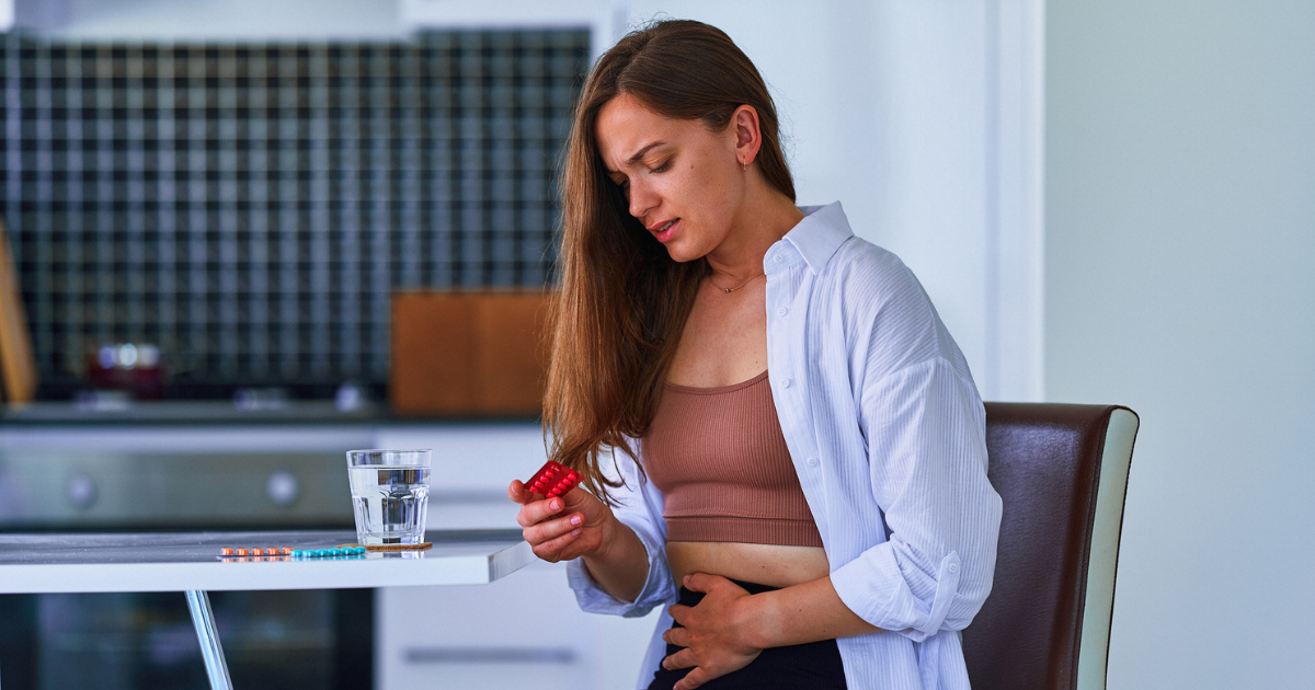 Woman grabbing her abdomen in pain, holding pills