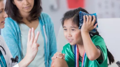 Picture of a young girl in a soccer uniform holding her head