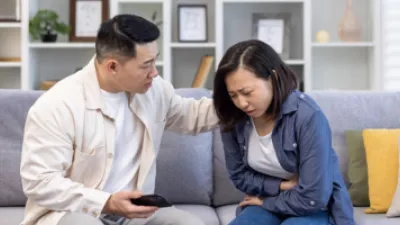 Woman holding her stomach in pain on the couch next to a man