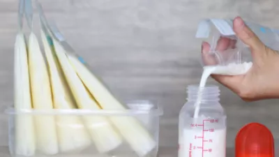 Close up of a hand pouring breast milk from a storage bag to a baby bottle