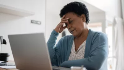 Woman sitting in front of her laptop and holding her head in pain