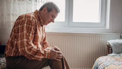 Older man sitting on a bed, holding his knee