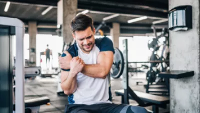 Man sitting on a weight bench and grabbing his shoulder in pain