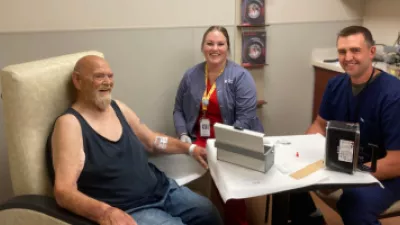 Craig Johnson, MD, Nuclear Medicine (right), and Beth McCaw, lead nuclear medicine technologist (center), administer the initial PLUVICTO dose to Phil Painter (left).