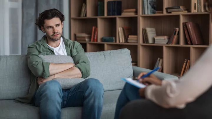 Man holding a pillow, sitting on couch in counselor's office