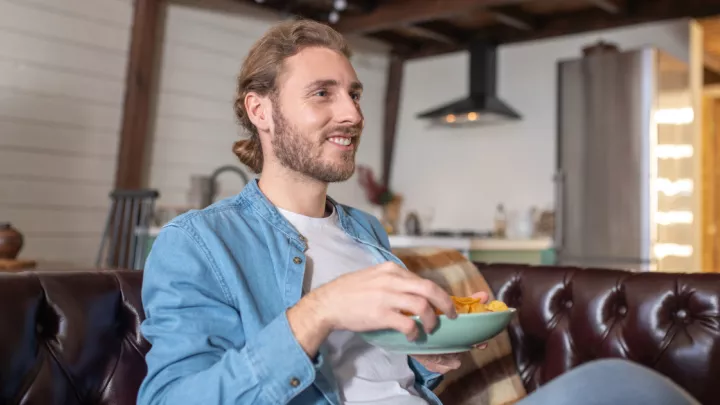 Man sitting on couch eating from bowl of chips