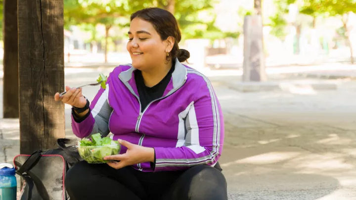 Woman sitting on the sidewalk and eating a salad