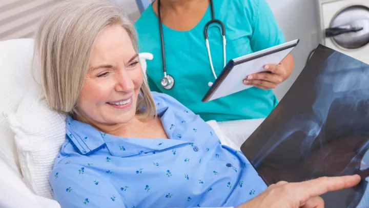 Woman in hospital bed looking at x-ray of hip replacement