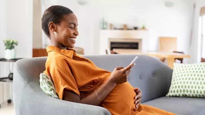 Pregnant woman sitting on the couch holding her phone