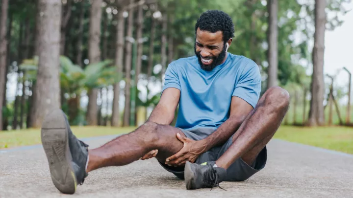 Man sitting on the ground holding his thigh in pain