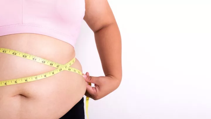 Woman holding tape measurer over stomach