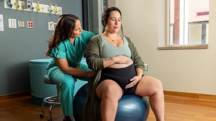Pregnant woman on exercise ball with midwife kneeling beside her