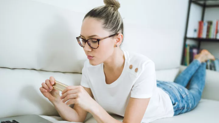 Woman laying on her couch looking at a pack of birth control pills