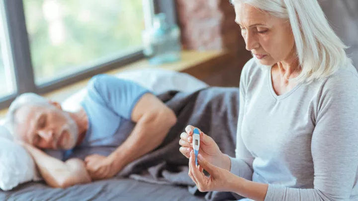 Sick man lying down and woman holding thermometer