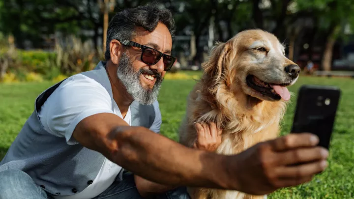 Man wearing sunglasses taking selfie with golden retriever