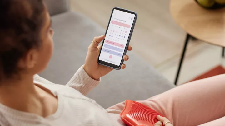 Woman with heating pad looking at calendar app on her phone