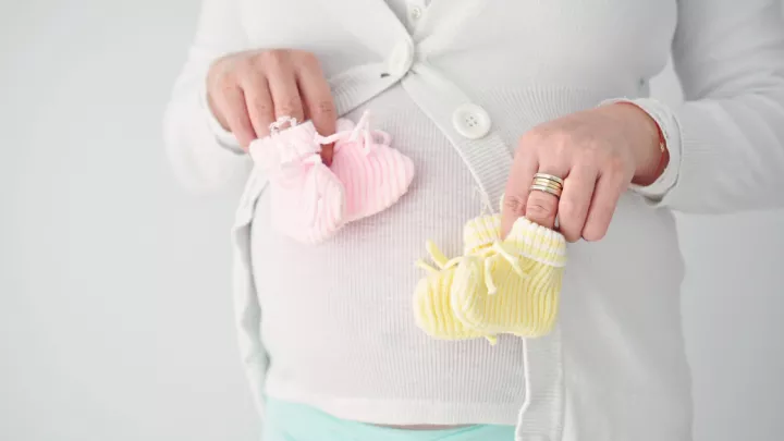 Pregnant woman holding two sets of booties in front of her stomach