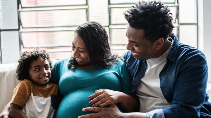 Father, pregnant mother, and young son sitting on couch