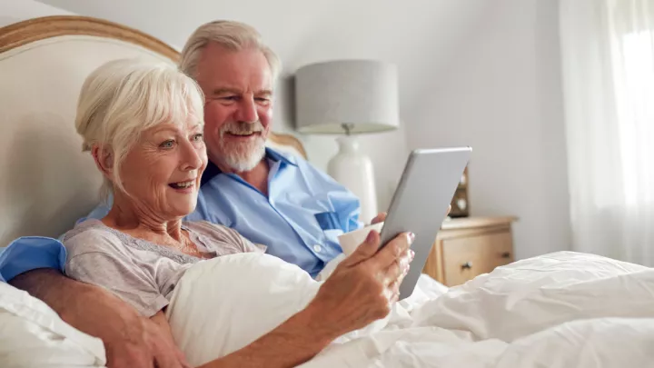 Older couple sitting in bed, looking at a tablet