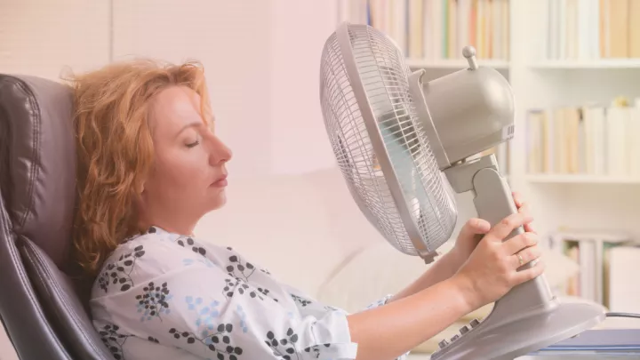 Woman sitting in an office chair and holding a desk fan to her face